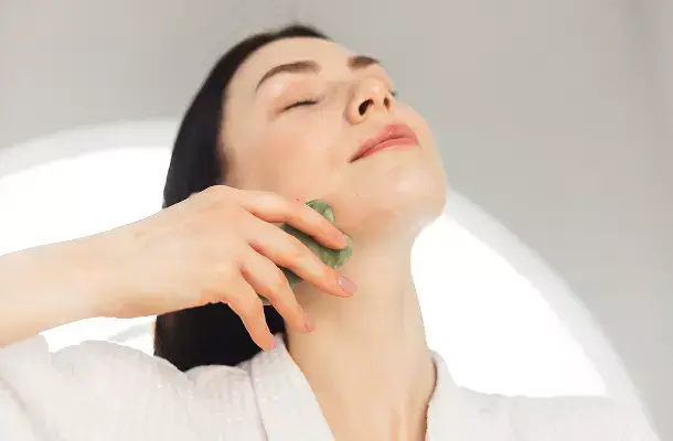 Een vrouw gebruikt een gua sha-steen bij haar kaaklijn.