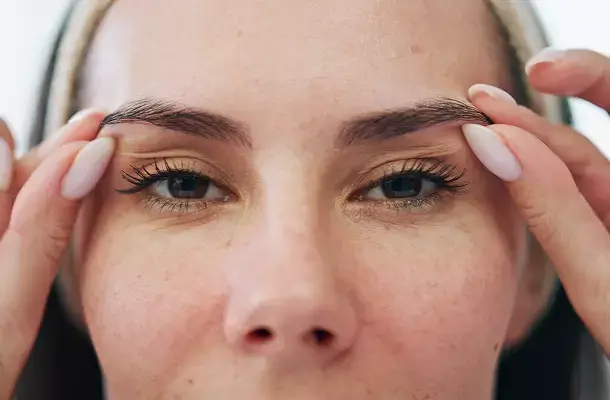 Een vrouw kijkt in de camera en trekt haar wenkbrauwen omhoog met haar vingers.
