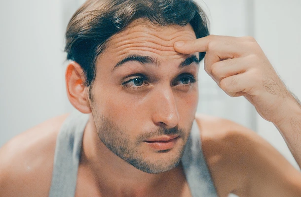 Een man fronst zijn voorhoofd en bestudeert zijn rimpels in de spiegel